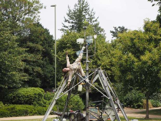 A performer in khaki suspended from an urban frame
