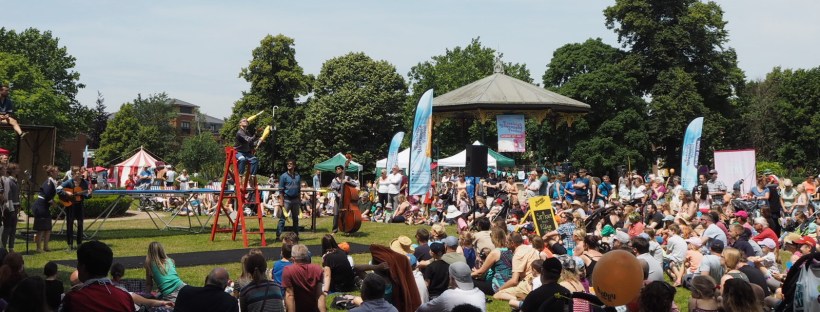 Street theatre festival; acrobats perform on a trampoline in front of a crowd, in the sun