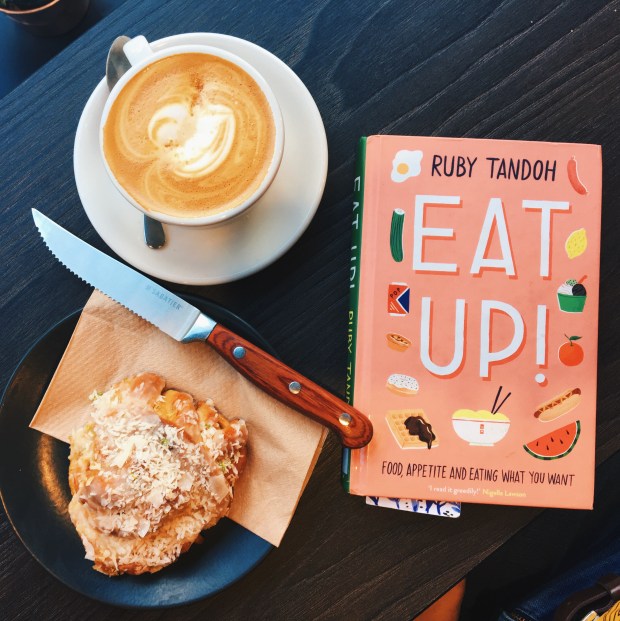 Ruby Tandoh's book, Eat Up, on a table with a coffee and an iced bun