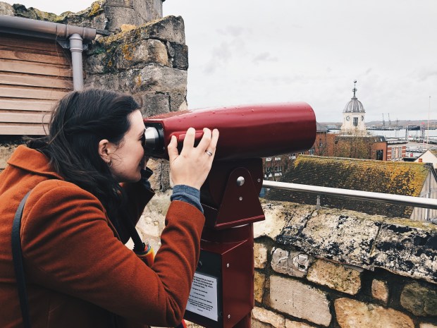 A brunette woman looking through tourist binoculors from the roof of the tower