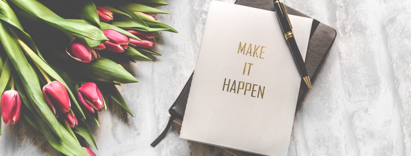 Tulips on a table next to a notebook with 'make it happen' on the cover