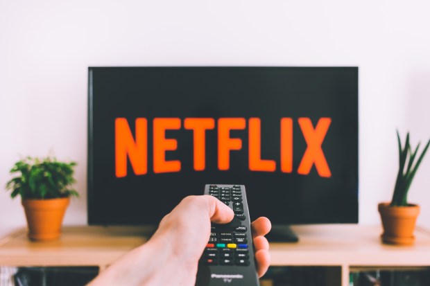 A hand pointing a TV remote at a TV with 'Netflix' on it.